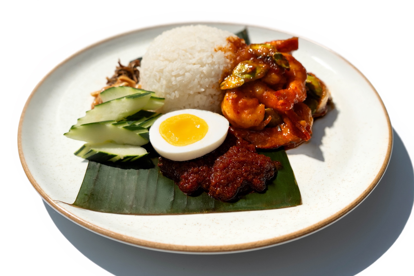 Nasi lemak platter — coconut rice, sambal prawns, petai, egg, cucumber, anchovies, and peanuts on banana leaf