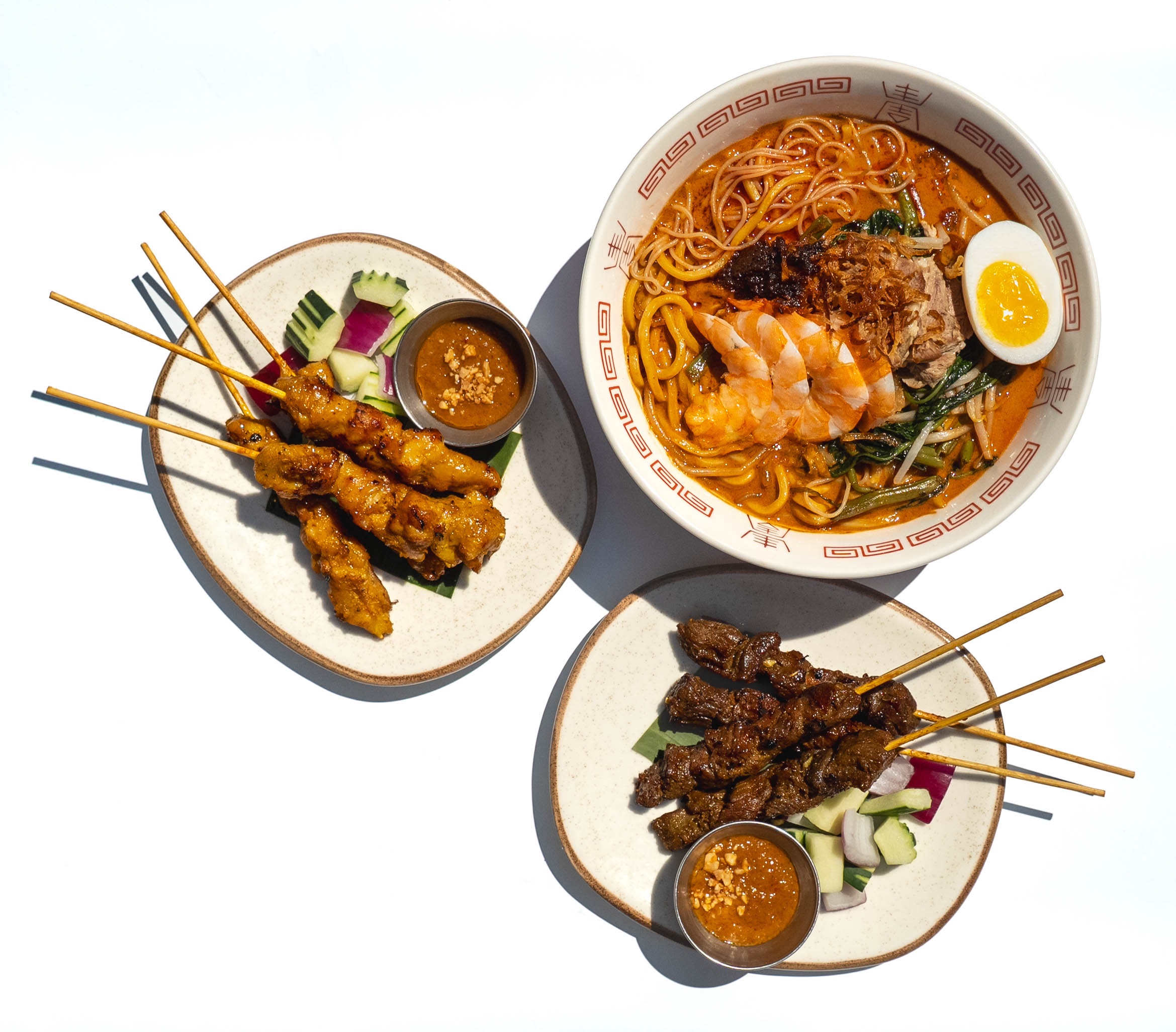 Chicken and beef satay platters with peanut sauce beside a bowl of curry laksa